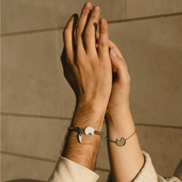 Couple wearing matching bracelets with charms, AN JEWELS JEWELRY Mod. AV.BMGLB05S, raising hands in sunlight.