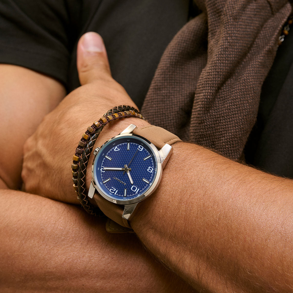 Close-up of a man's wrist wearing a stylish blue-faced round watch and a brown beaded bracelet, showcasing fashion accessories.