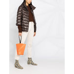 Woman wearing Herno Jackets Brown with padded design, high neck, and 3/4 sleeves, holding an orange bag, styled with light pants.