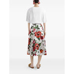 Back view of woman wearing white shirt and floral midi skirt with red and green pattern, holding hands by side, standing against white background.