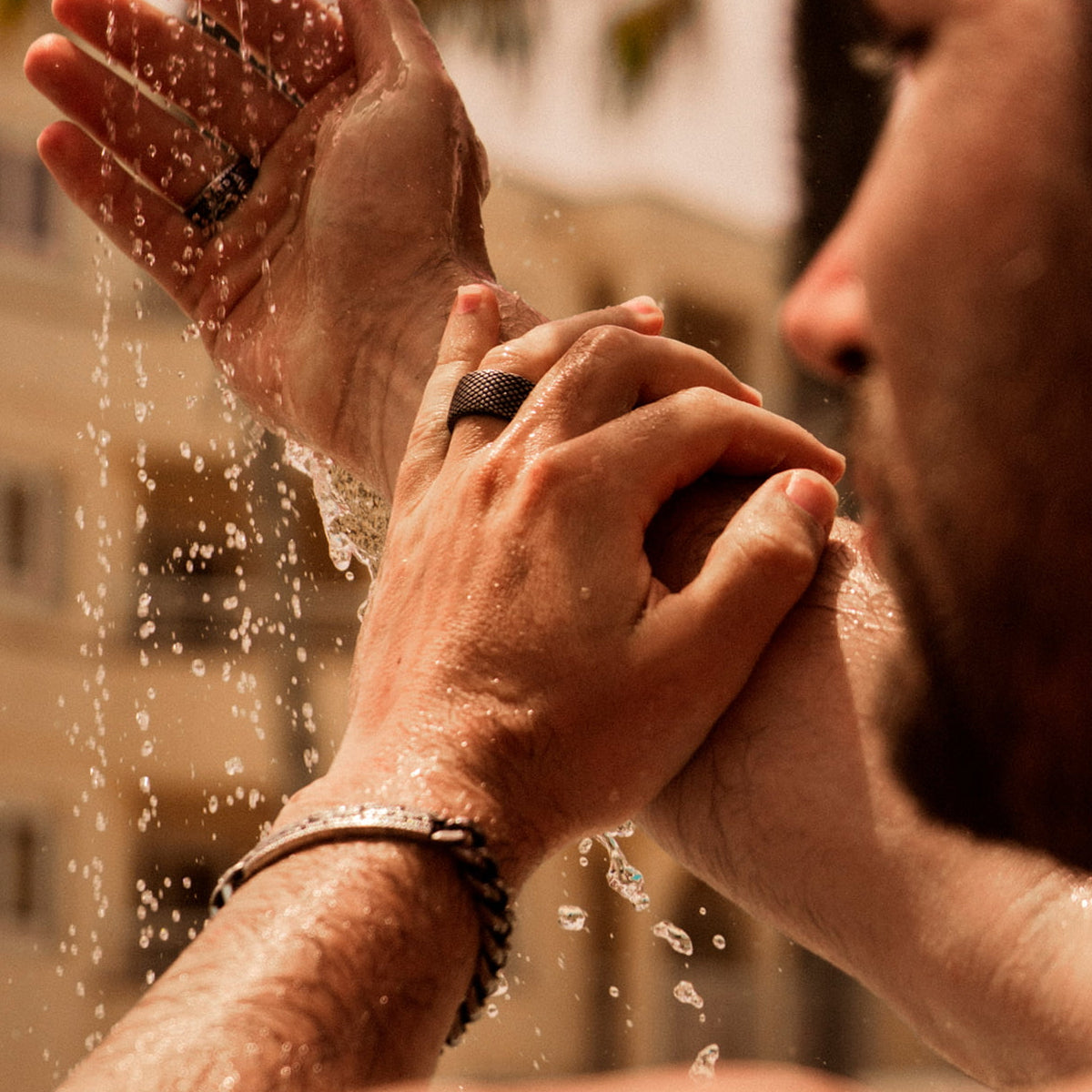 Man wearing rings washing hands outdoors, showcasing AN JEWELS JEWELRY Mod. AA.R01A-10 under flowing water.