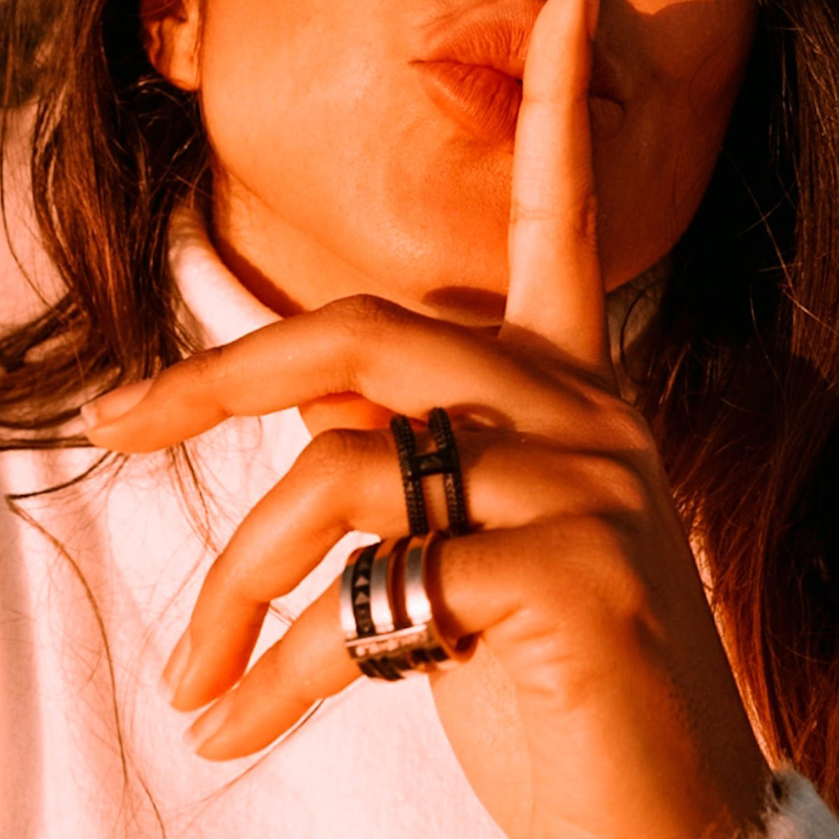 Woman wearing rings from AN JEWELS JEWELRY Mod. AR.R2NS02BK-9 collection, with a finger to her lips in a shushing gesture.