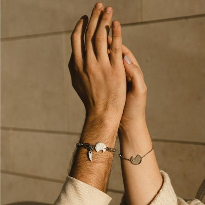 Couple wearing matching bracelets with charms, AN JEWELS JEWELRY Mod. AV.BMGLB05S, raising hands in sunlight.
