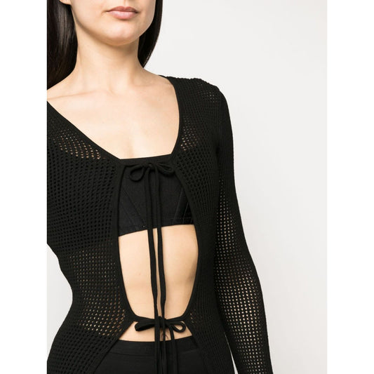 Model wearing ANDREĀDAMO Andrea Adamo Sweaters Black, semi-sheer knitted cardigan with racerback and front tie fastening.