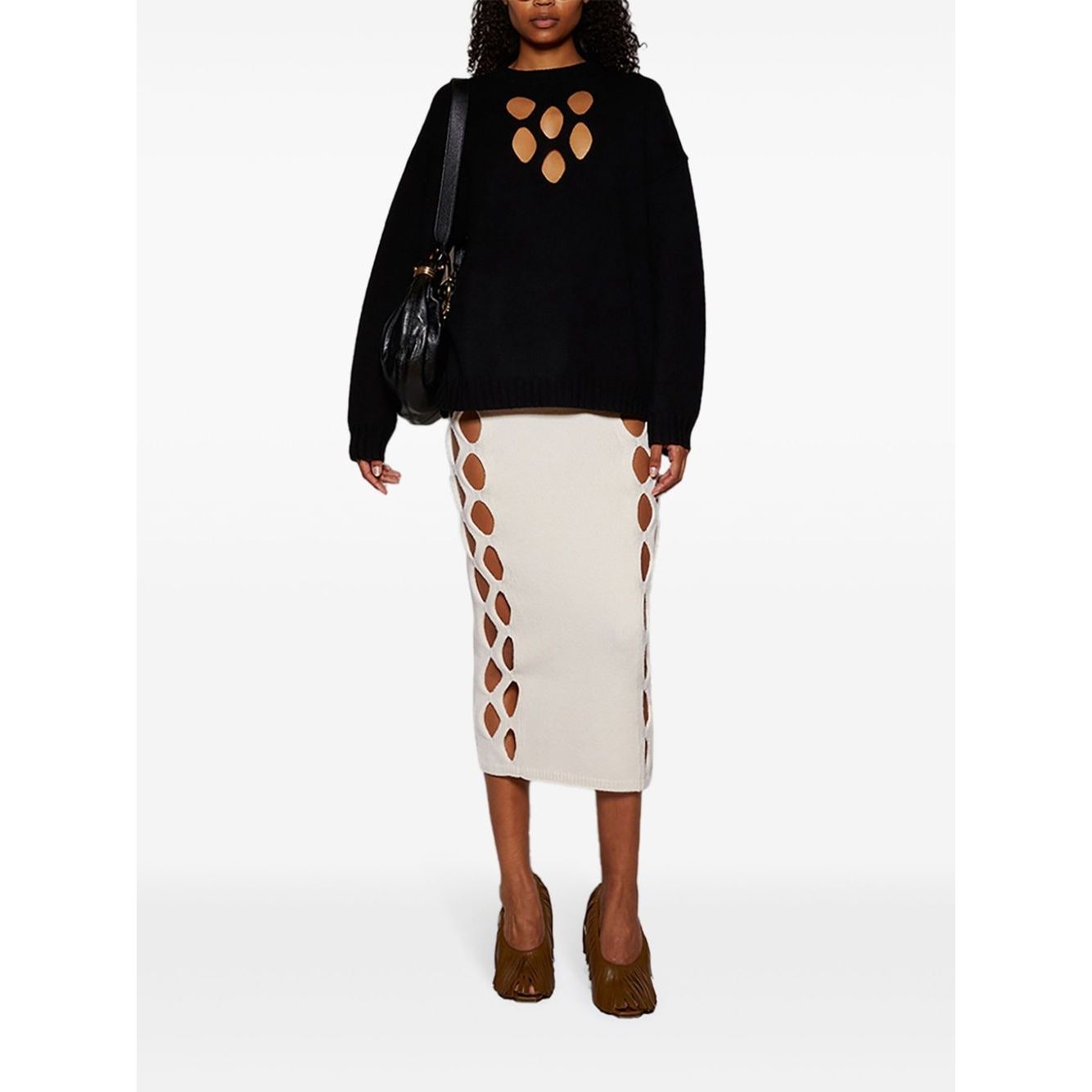 Fashion model wearing black sweater, cream cutout skirt, and carrying Chloé Small Bracelet Hobo Bag.