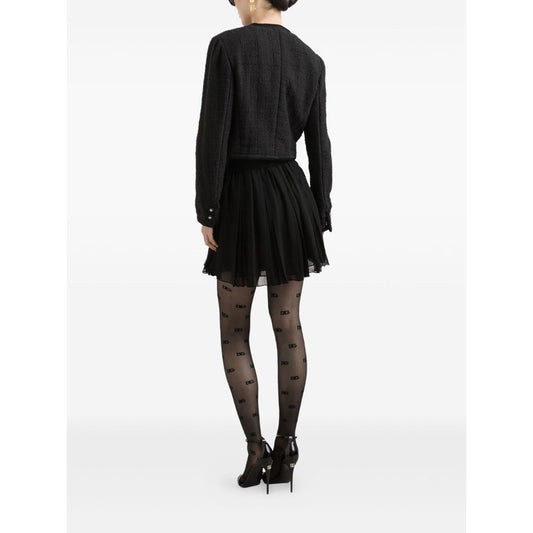 Back view of model wearing Dolce & Gabbana Rachel Tweed Jacket, black crew neck, buttoned cuffs, with a pleated skirt and patterned tights.