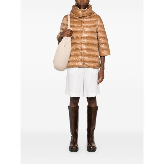 Model wearing Herno Jackets Camel with quilted design, stand-up collar, three-quarter sleeves, paired with white shorts and brown boots.