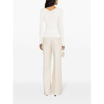 Back view of model wearing JACQUEMUS Top White with long sleeves and scallop edge, paired with neutral pants, showcasing V-neck and ribbed design.