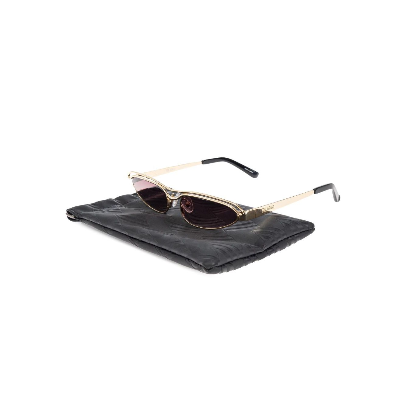 The Attico Norma sunglasses with gold-tone UV-protective lenses, logo-engraved arm, and curved tips on a black case.