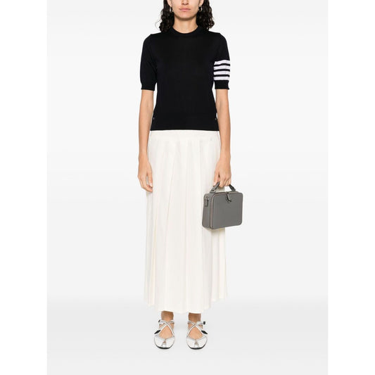 Person wearing navy Thom Browne Sweaters Blue with 4Bar wool design and grosgrain tab, paired with a white skirt and holding a gray handbag.