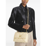 Woman wearing a black jacket carrying a Tory Burch Kira Diamond small leather shoulder bag in light yellow with a gold chain strap.