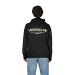 Man wearing the Underclub Black Cotton Sweater with hood and ribbed cuffs, displaying back view, text "Brooklyn, NY" visible.