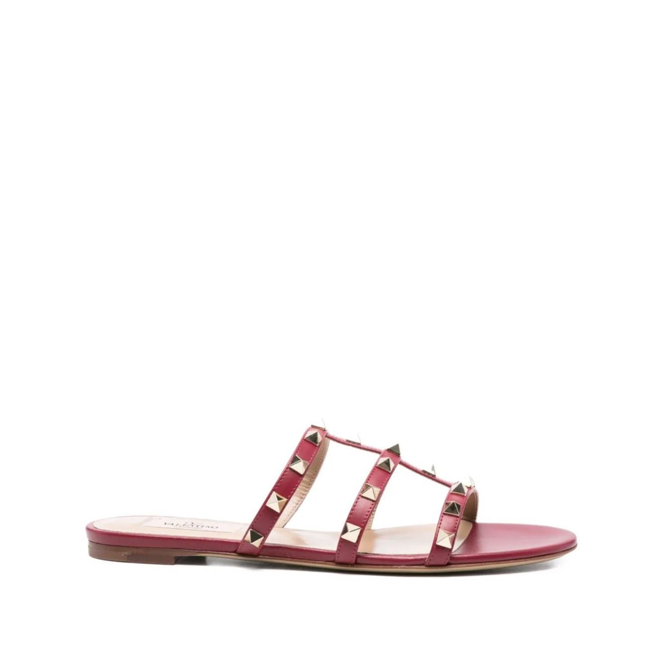 Valentino Garavani Rockstud three-strap sandals in red calf leather with flat sole, open toe, and signature studded embellishments.