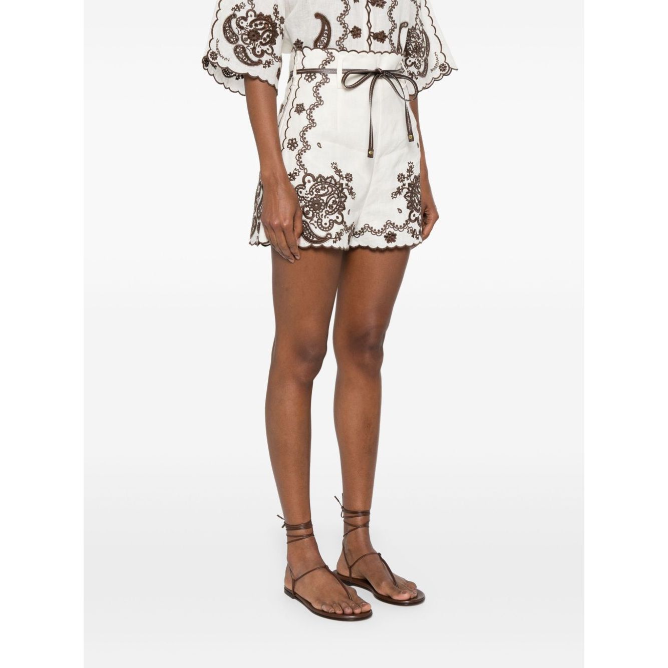 Zimmermann Ascension Shorts in light beige linen with scallop edge embroidery and detachable belt, modeled outdoors.